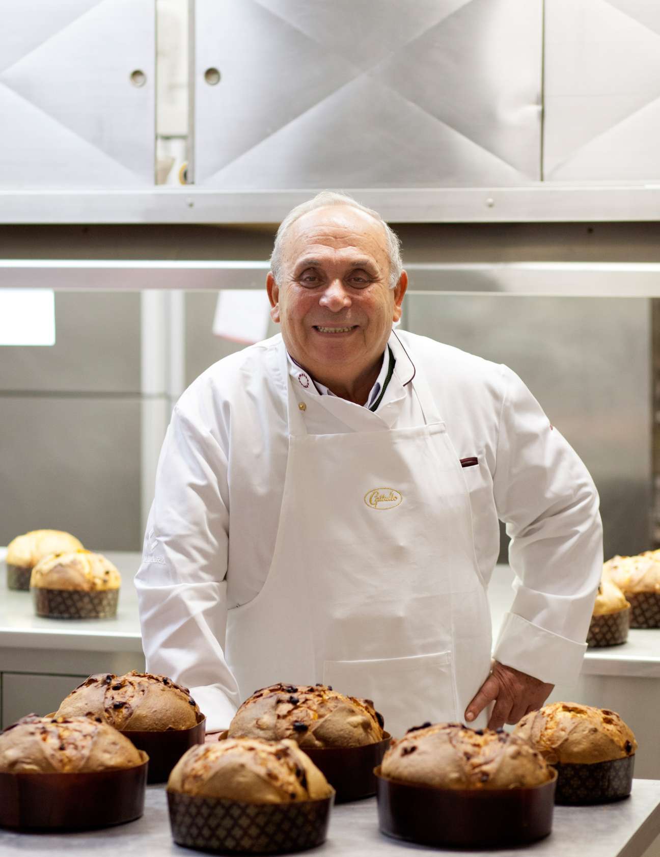 A baker in white Gattullo apron stands behind panettone loaves in a modern kitchen.