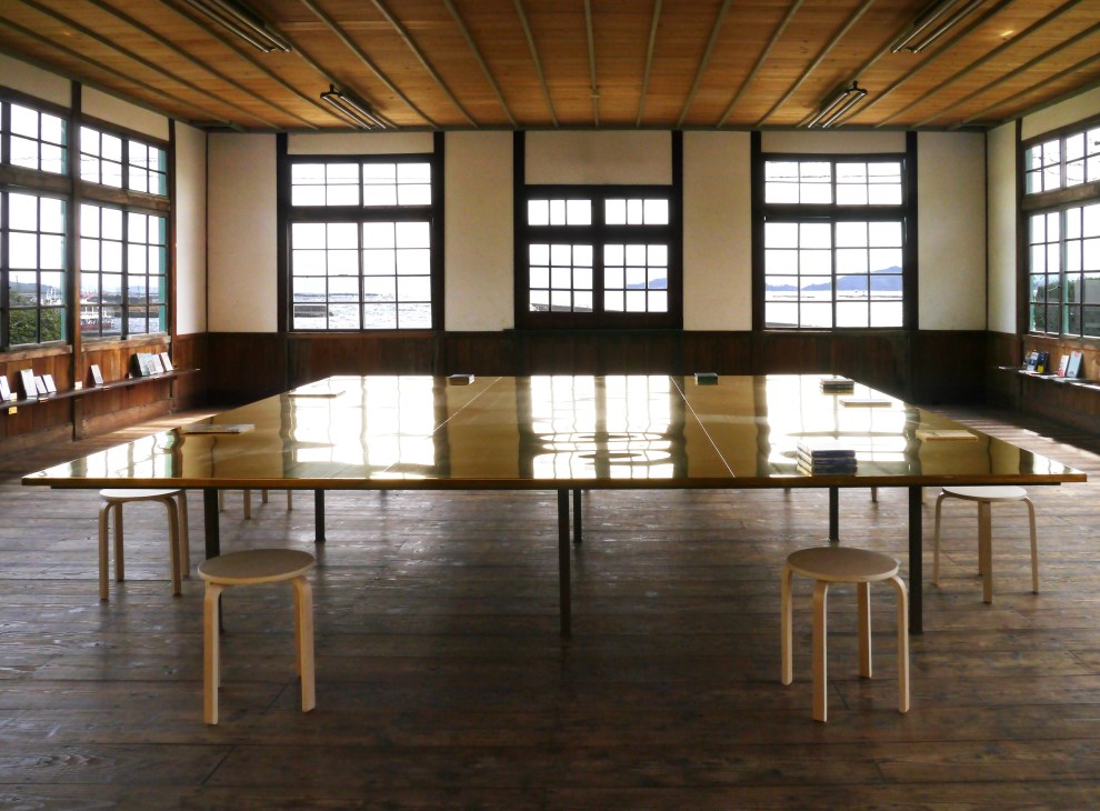 Refurbished 1920s wooden seamen's school library on Awashima island with brass reading table, large windows and sea views.