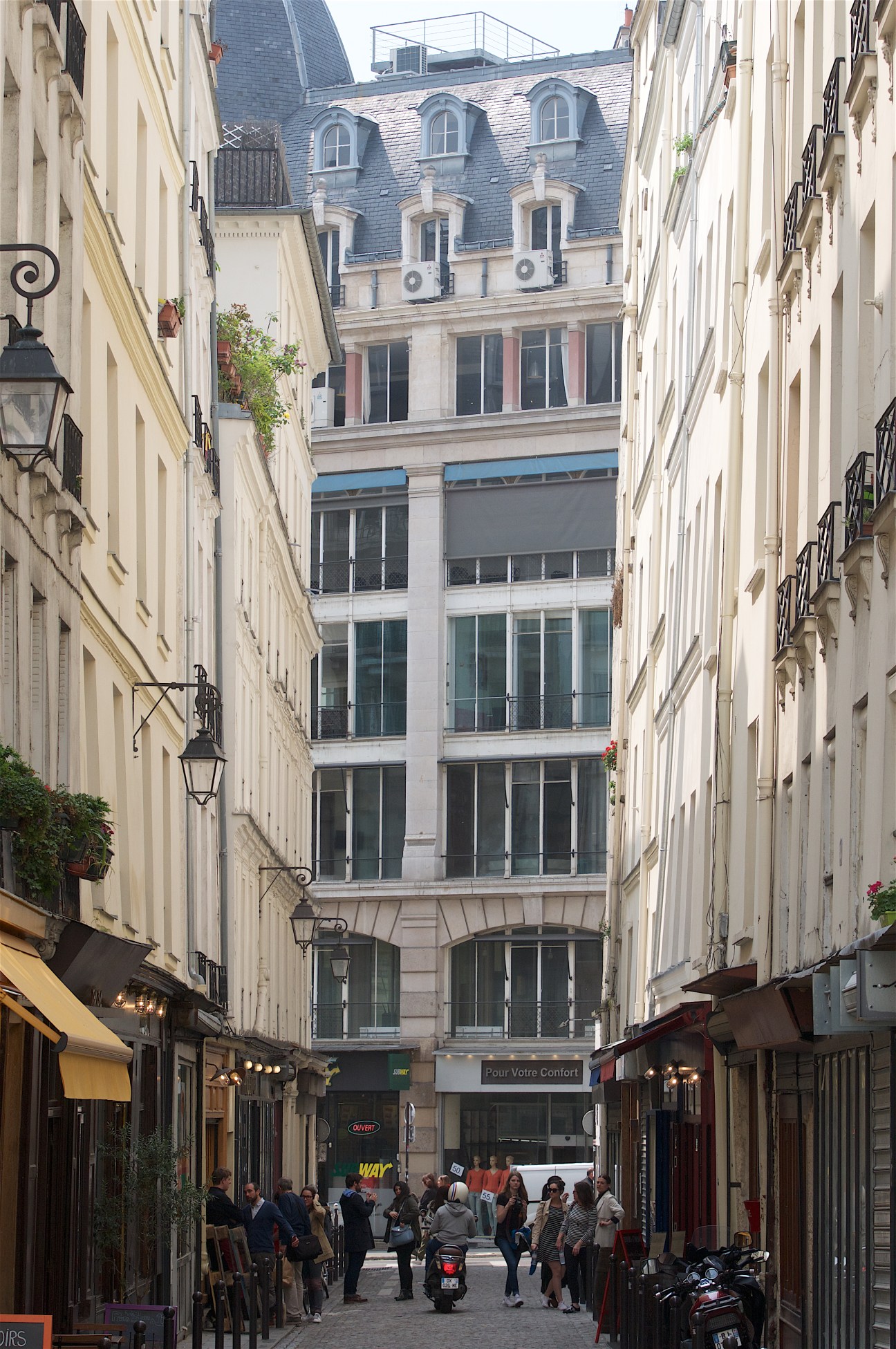 Narrow Parisian street lined with historic buildings and small shops, with pedestrians walking through the passage.