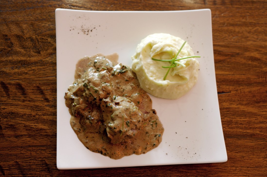 Seasoned steak with mashed potato garnished with chives on a white plate.