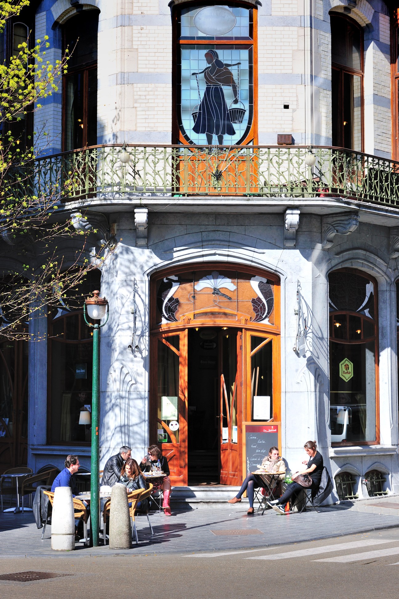 Bar La Porteuse d'Eau storefront with art nouveau facade, ornate railings, and customers seated outside in Saint-Gilles, Brussels.