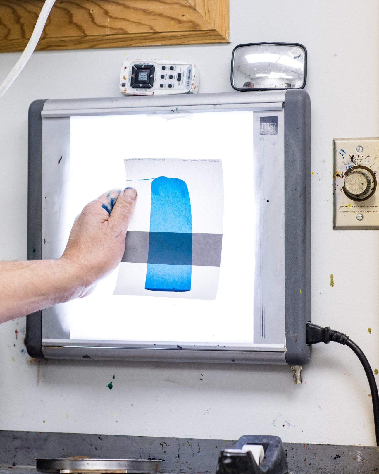 A hand holds a printed color sample showing blue and gray geometric shapes against a lightbox for shade matching.