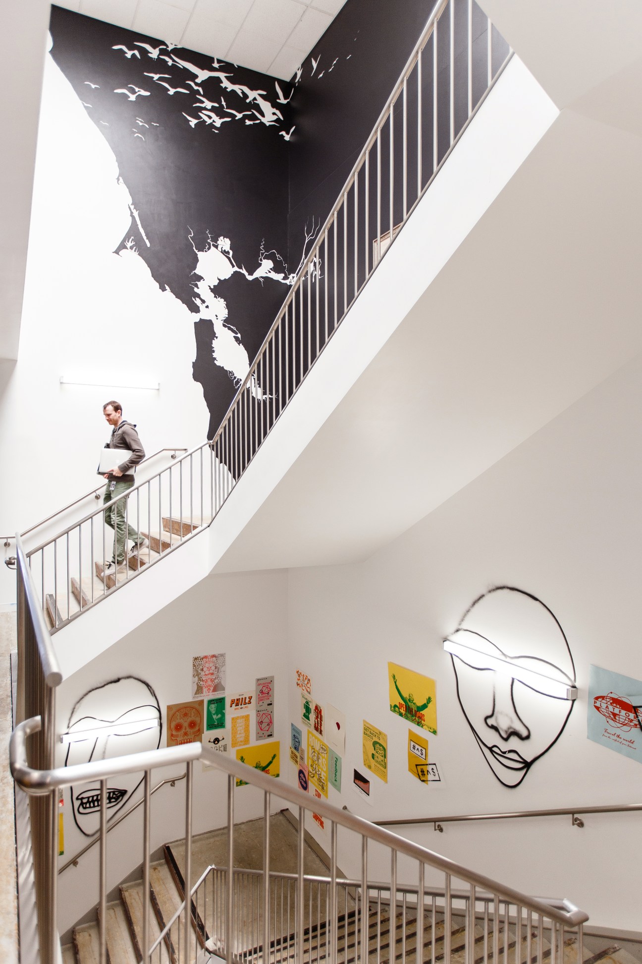 Man walking up spiral staircase past artwork and neon face sculptures in Facebook office.