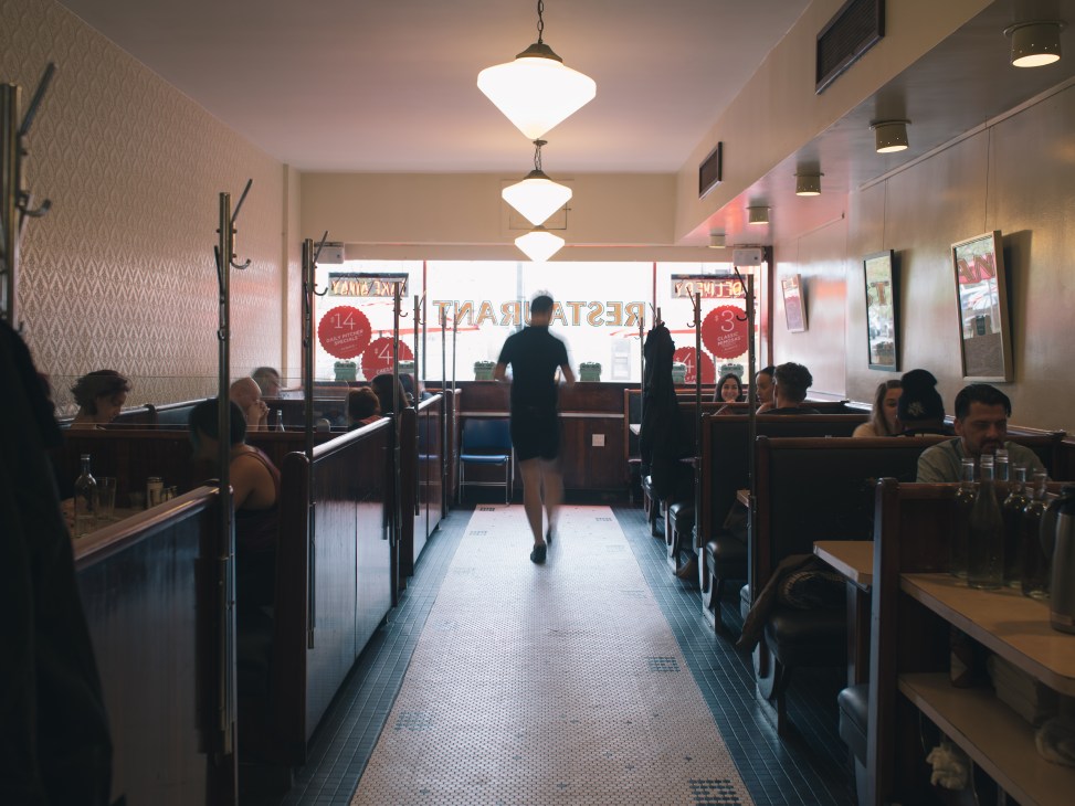 Interior of Lakeview Restaurant in Toronto showing diners seated in booths along a narrow aisle with pendant lighting overhead.