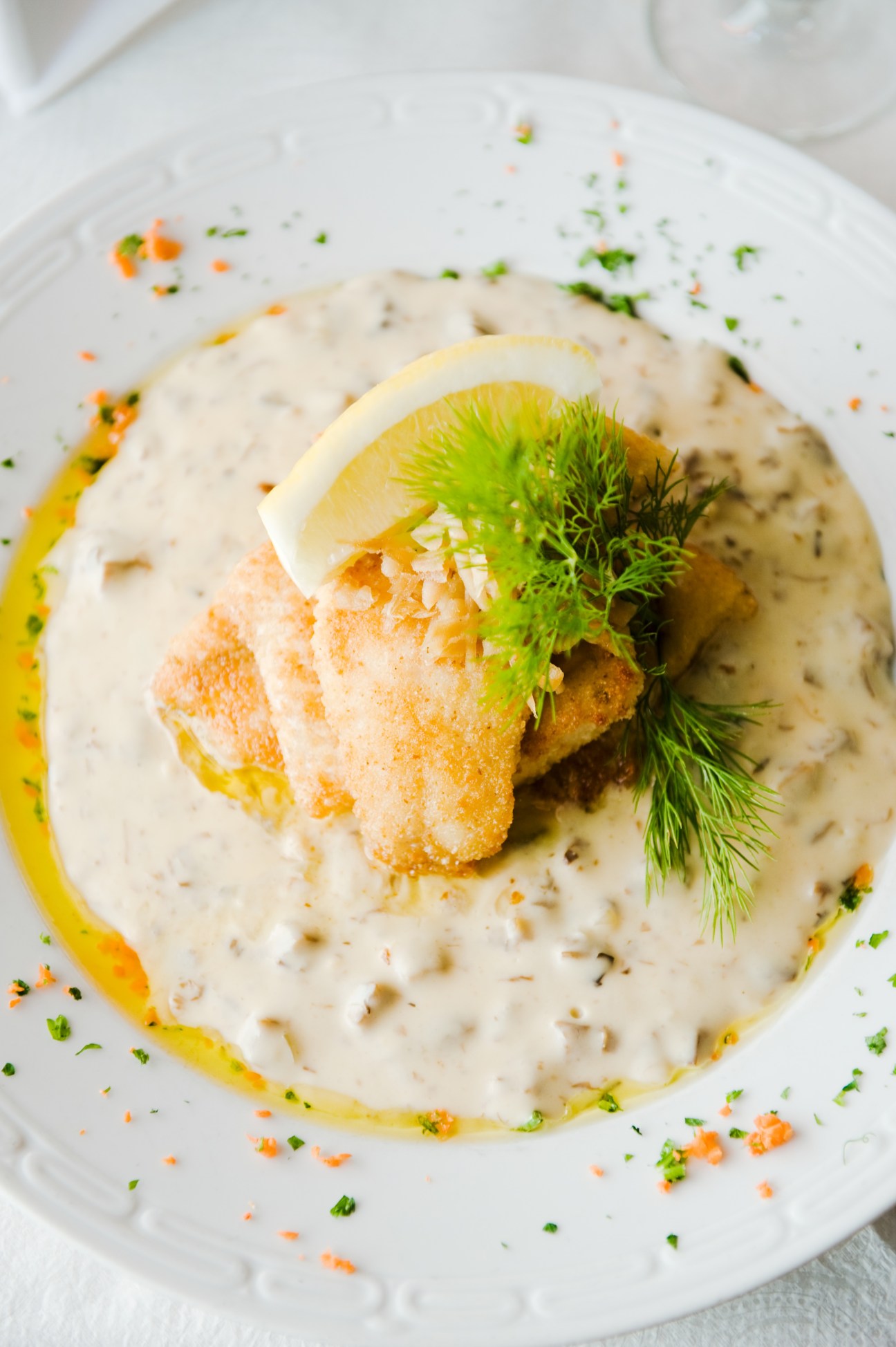 Plated white fish dish with creamy sauce, lemon wedge, fresh dill, and herb garnish on white plate.