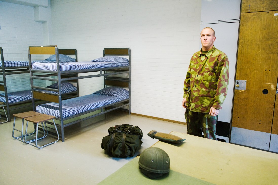 Finnish conscript Jan-Aley Johnson standing in military barracks with bunk beds and equipment.