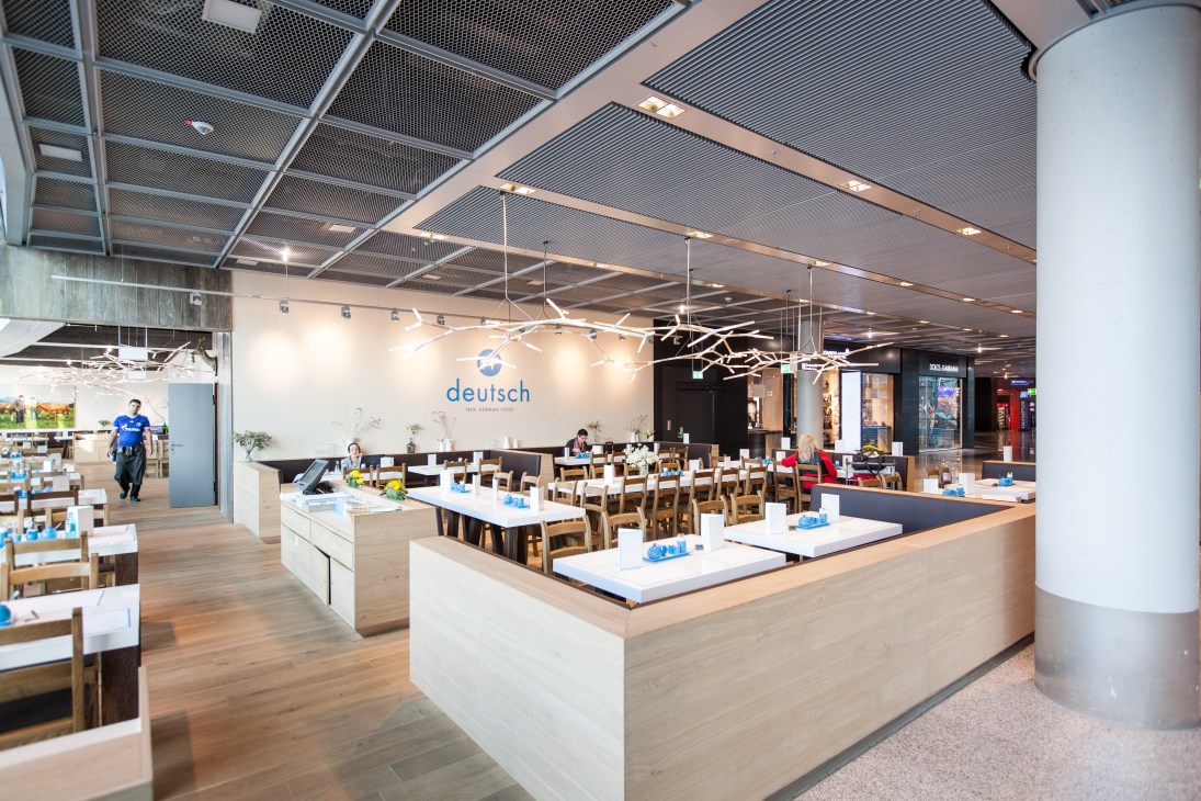 Interior of Deutsch restaurant at Frankfurt airport with modern seating, light wood tables, and blue signage.