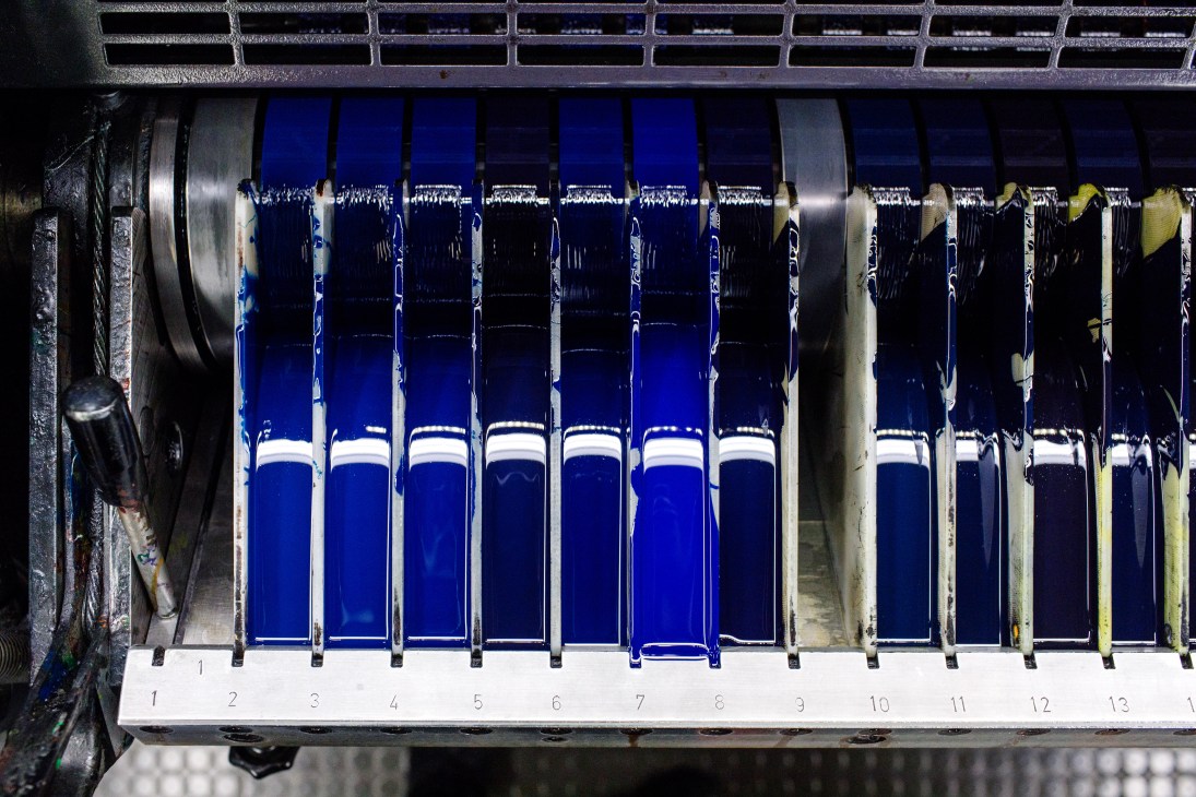 Numbered blue color samples displayed in a printing machine's drying rack for Pantone fan deck production.