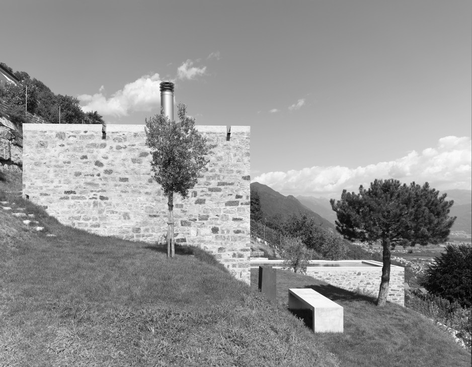 Modern stone house with panoramic mountain views and a minimalist bench in the foreground.