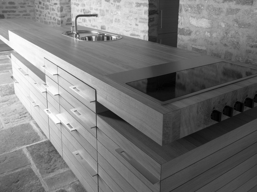 Modern kitchen with wooden cabinetry, stainless steel sink and cooktop in a stone interior.