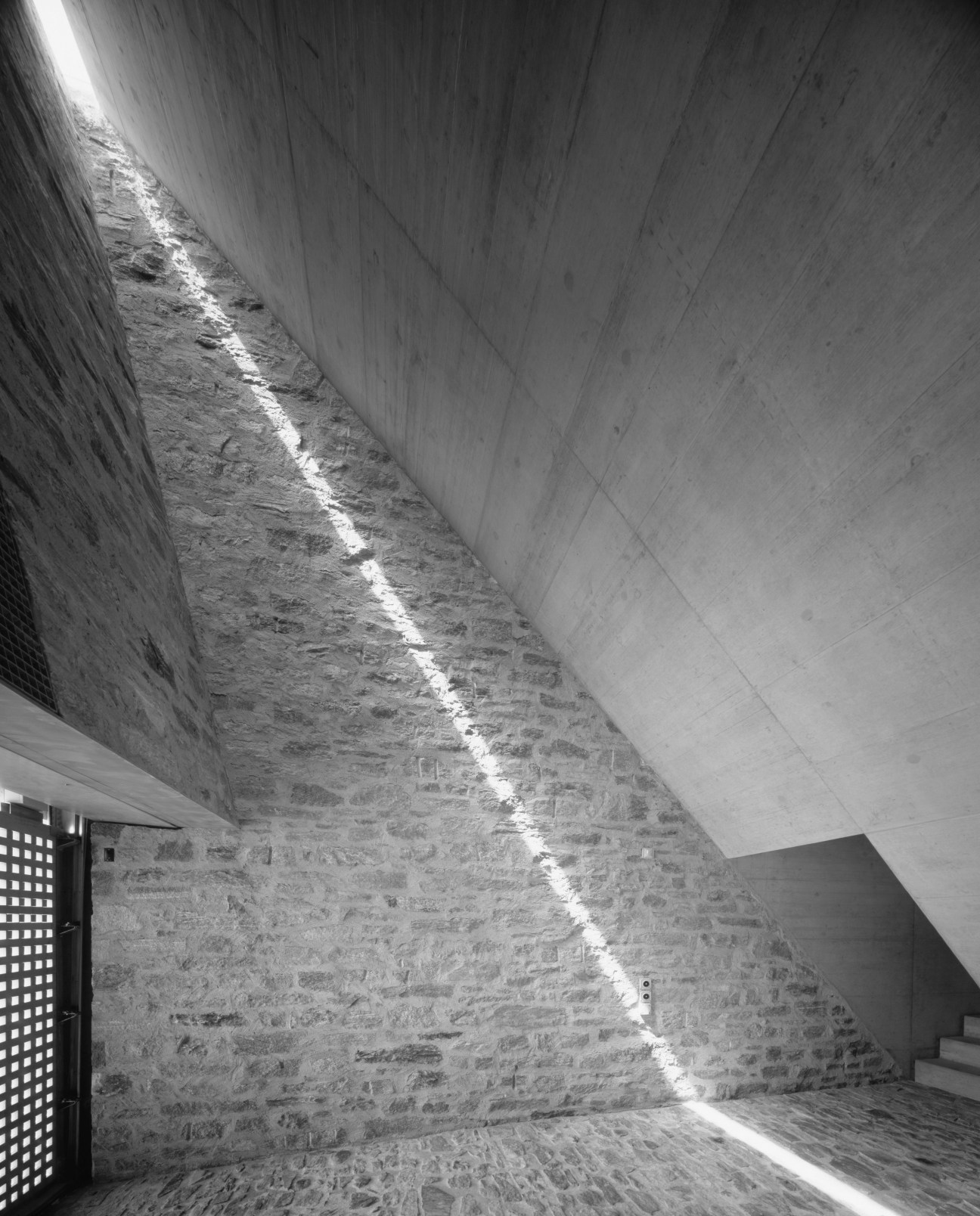 Interior of modernist stone house with angled concrete ceiling and natural light streaming through skylight