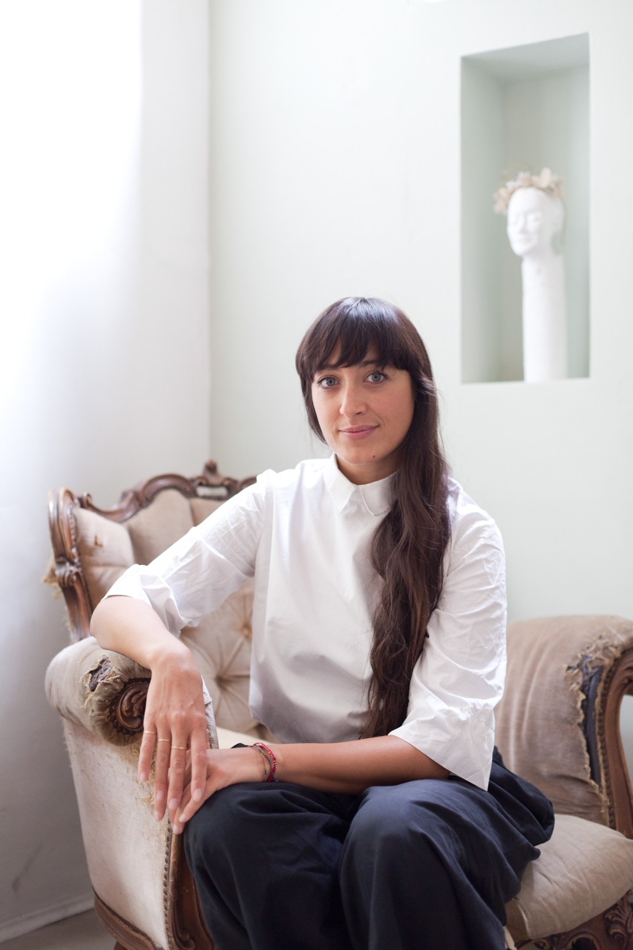 Elena Pignata, fashion designer and owner of boutique Ombradifoglia, sits on an upholstered chair in a minimalist interior.