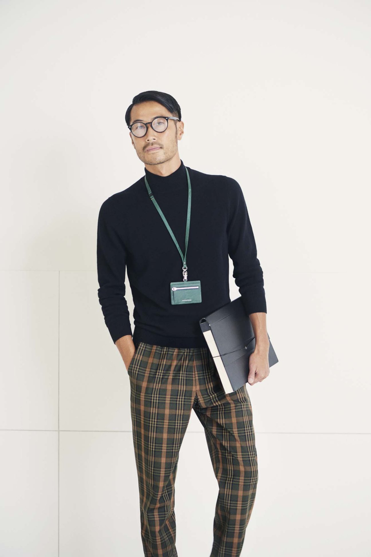 Man in black high-neck jumper by Bottega Veneta and plaid trousers by Barena Venezia wearing Ray-Ban glasses and Porter lanyard.