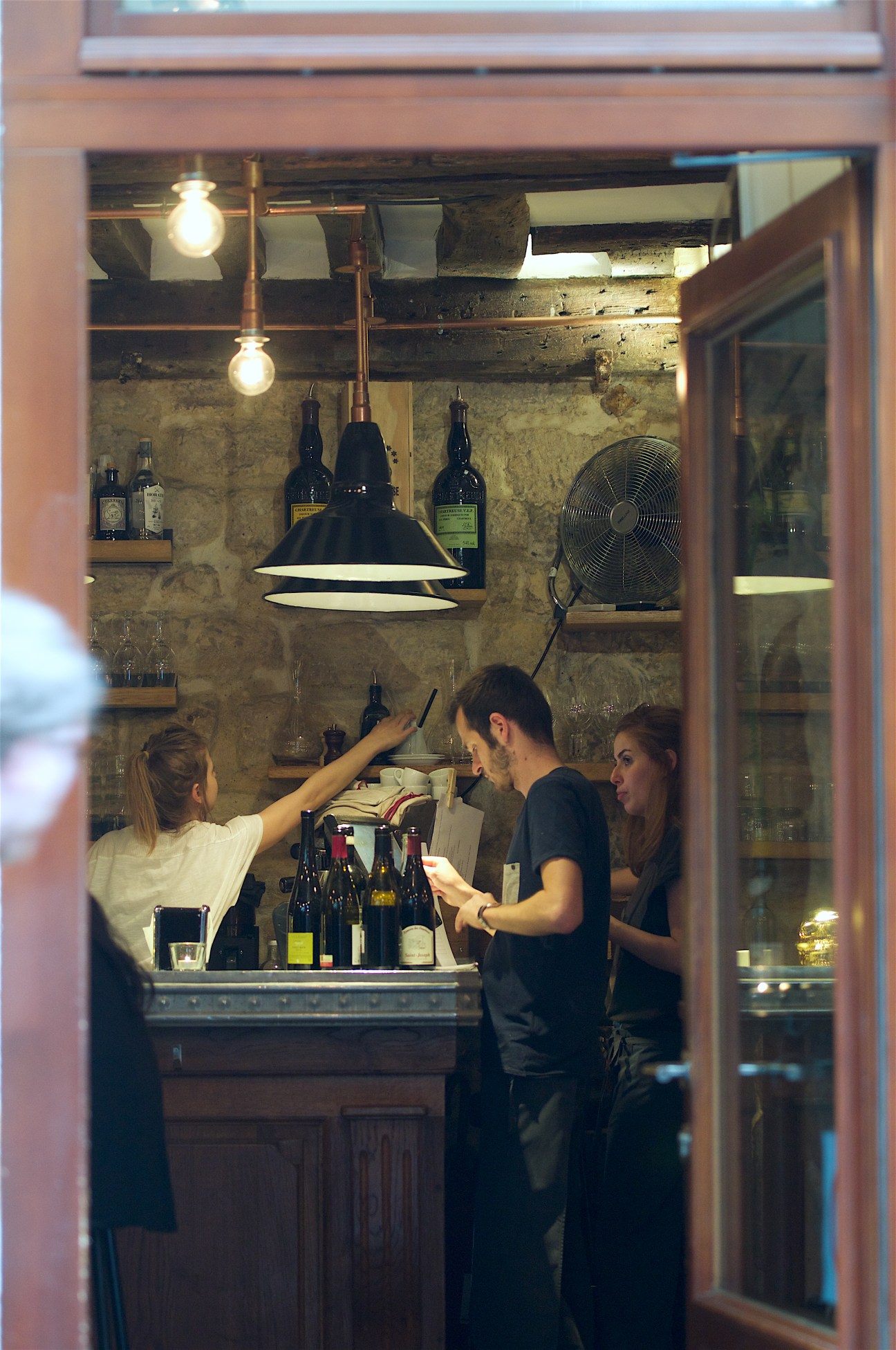Interior of Frenchie bistro with staff and wine bottles visible through window at dusk.
