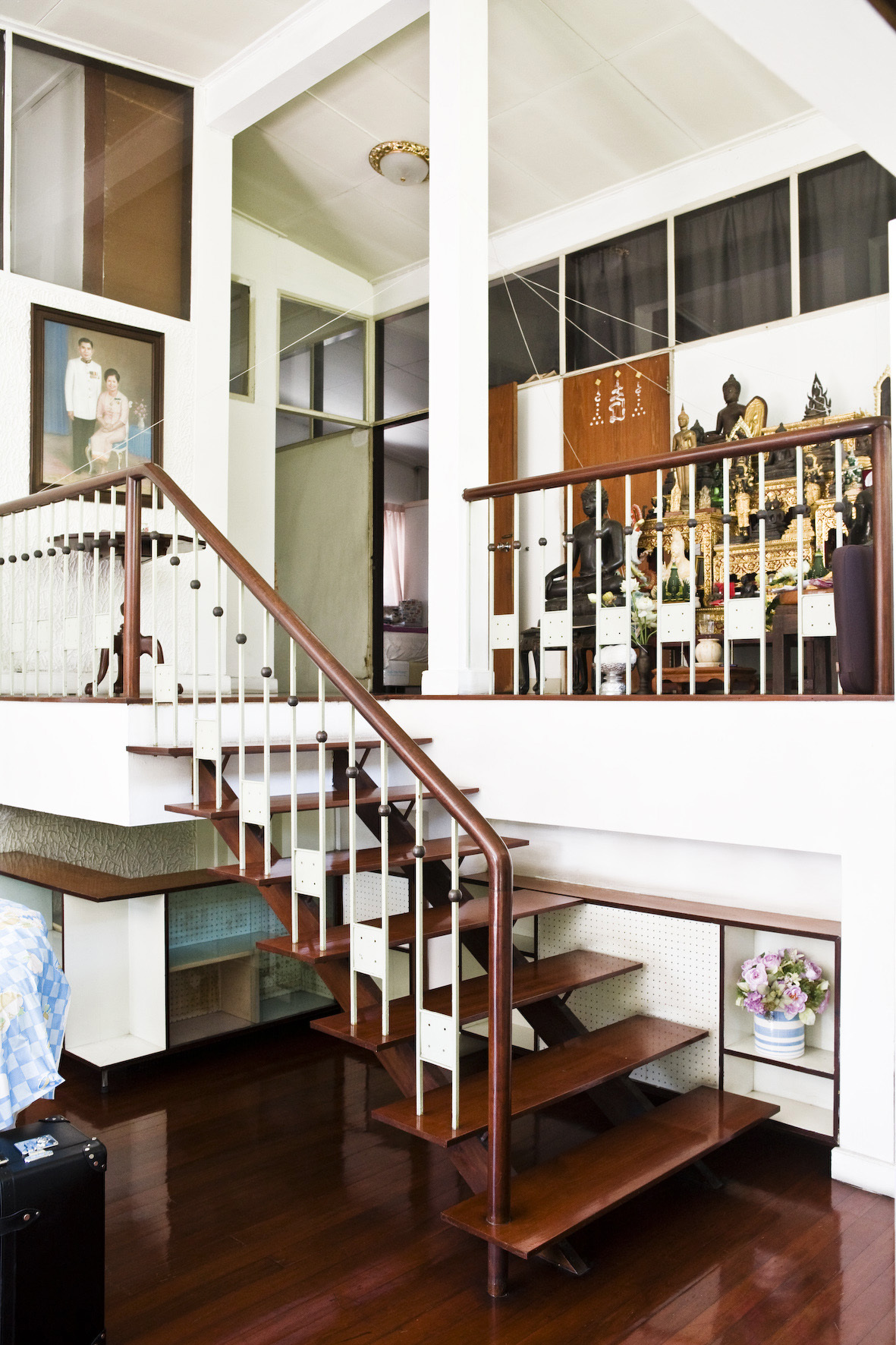 Interior staircase of a 50-year-old Bangkok residence with wood steps, white railings, and Buddhist altar.