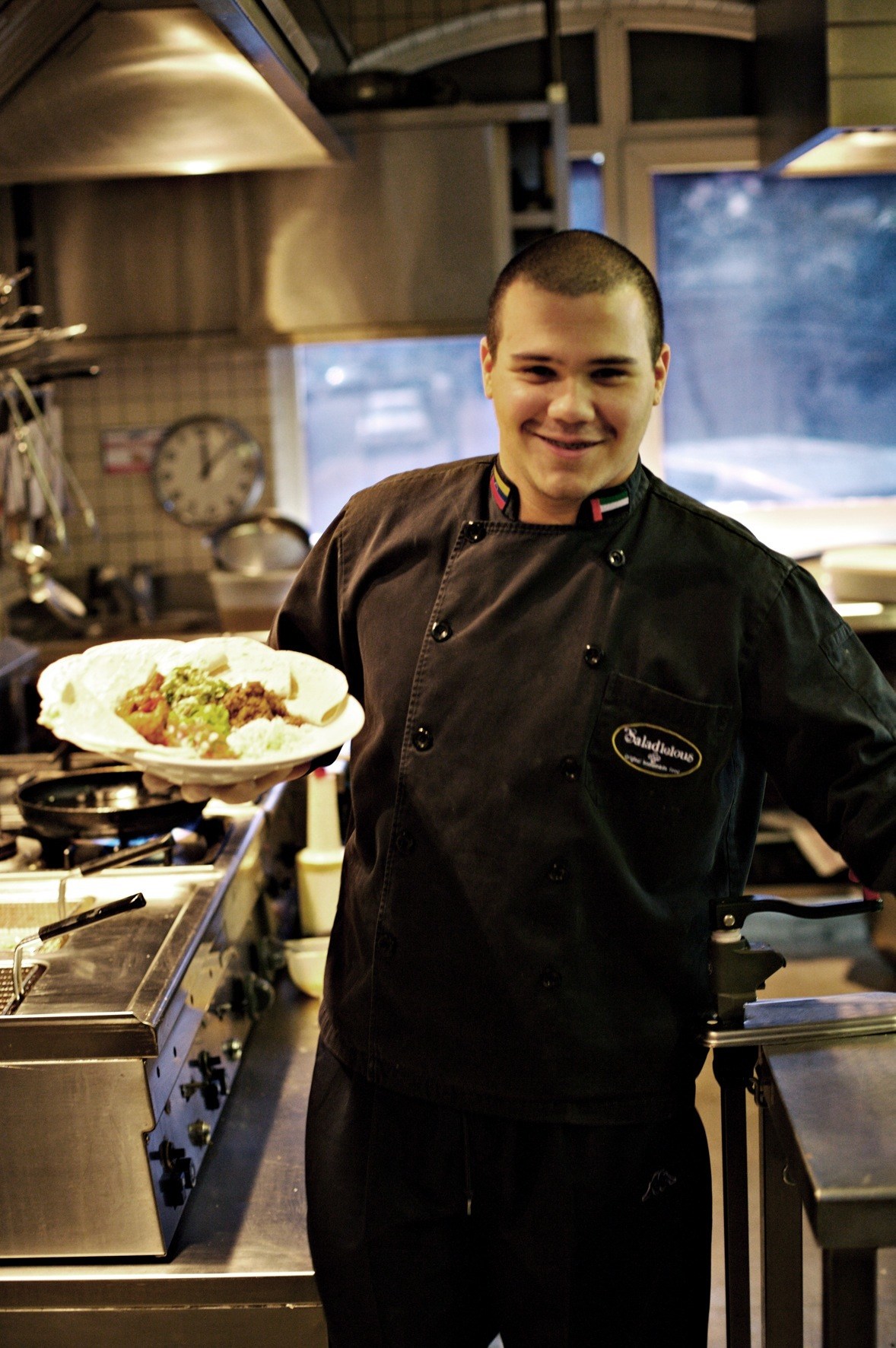 Venezuelan chef Isterling Eloy Alvarado holds a plate of fajitas in Saladicious restaurant kitchen.