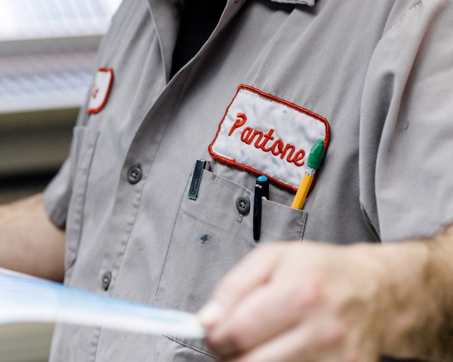 Pantone employee wearing a gray work shirt with a Pantone logo patch and pens in the pocket.