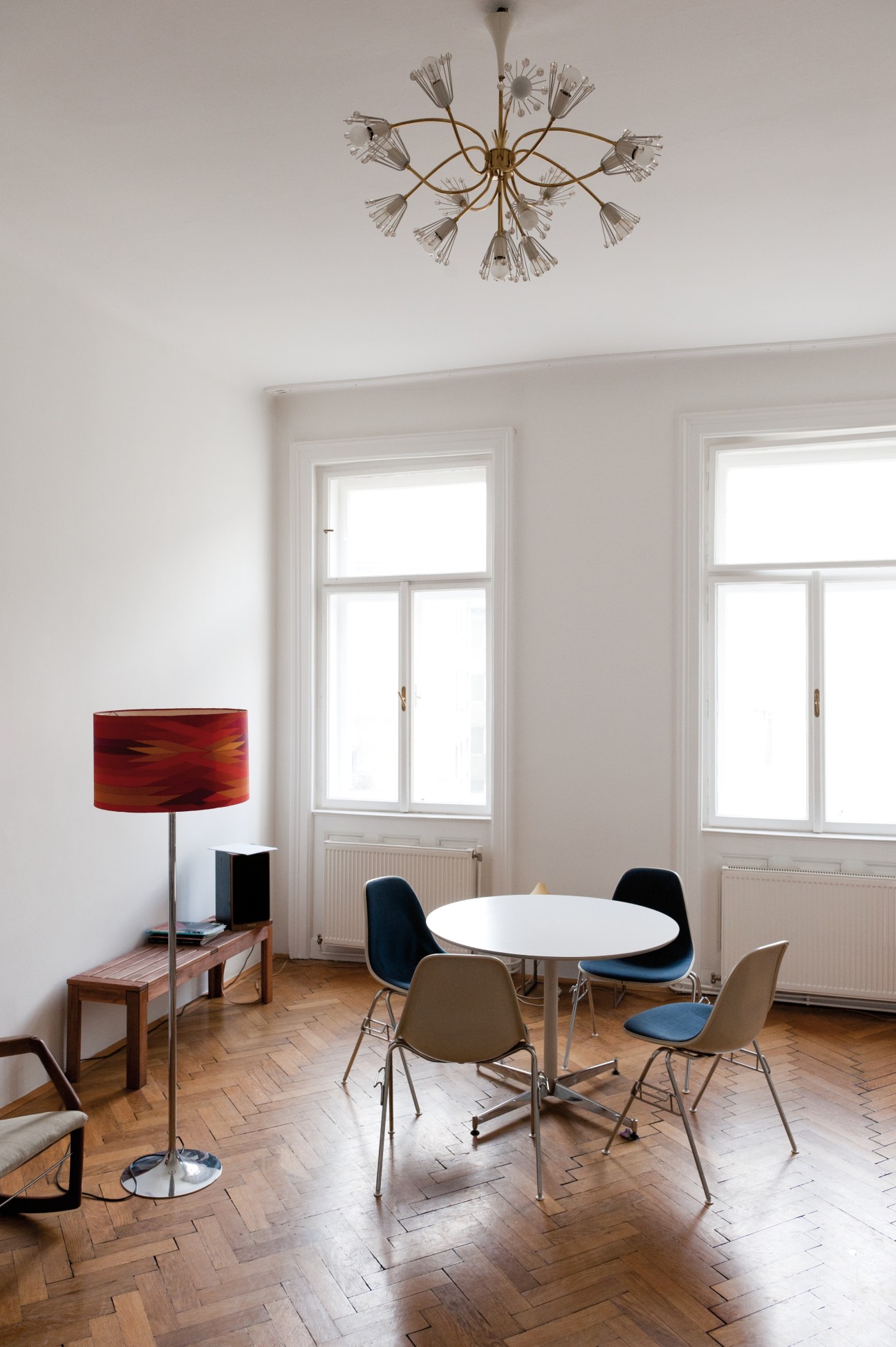 Modern dining room with round white table, mid-century chairs, brass chandelier, and herringbone wood floors.