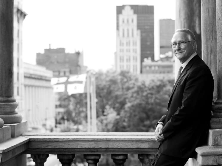 Gérald Tremblay, Mayor of Montréal, stands on a balcony overlooking the city skyline in black and white.