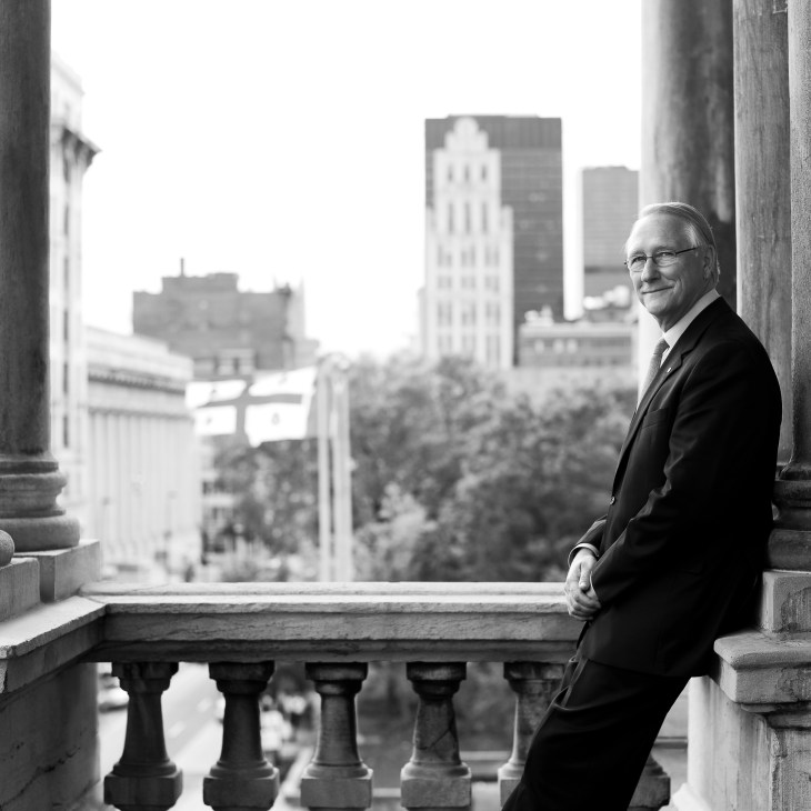 Gérald Tremblay, Mayor of Montréal, stands on a balcony overlooking the city skyline in black and white.