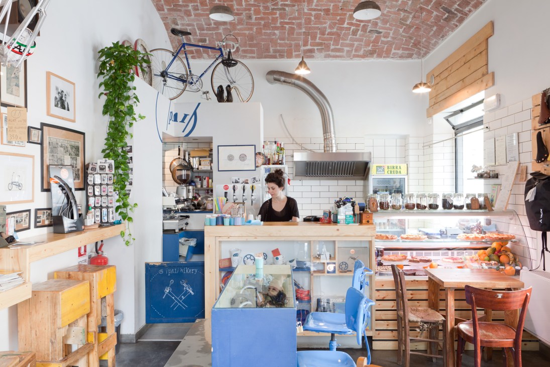 Interior of Pai Bikery bike shop and café with exposed brick ceiling, bicycle hanging on wall, and barista behind counter.