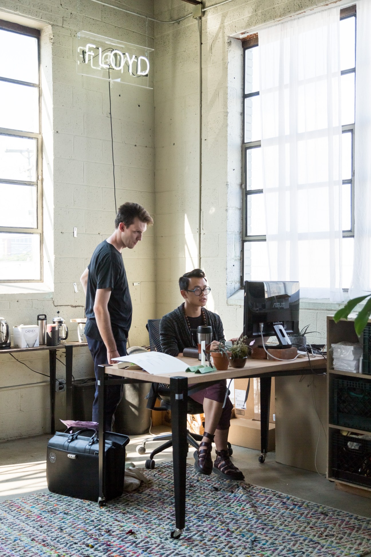 Two people work in a Floyd office space in Detroit's Corktown, with the Floyd logo visible on the wall behind them.