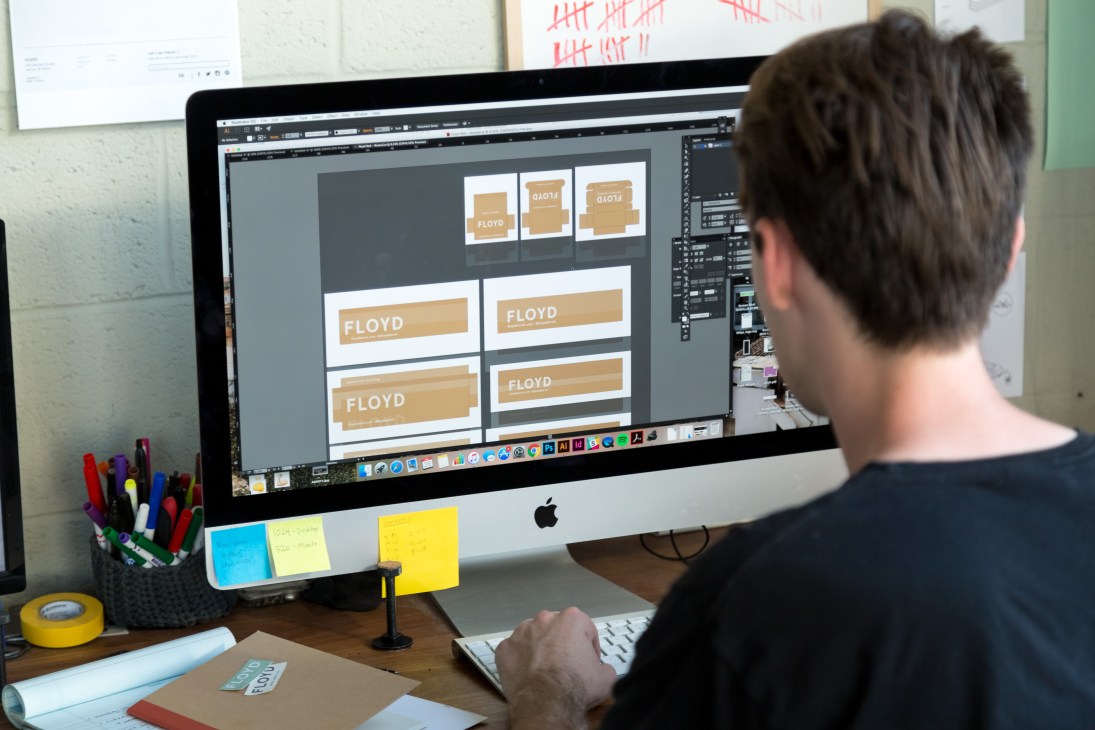Designer working at iMac displaying Floyd furniture brand packaging layouts
