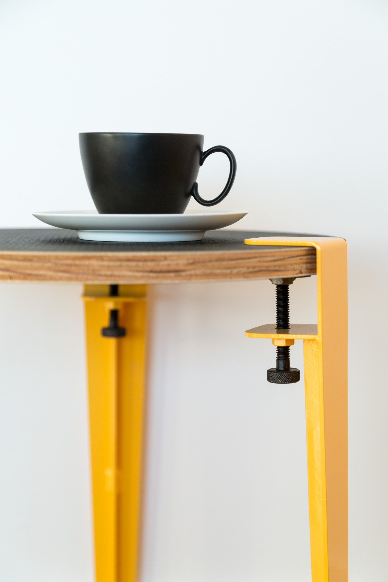 Black ceramic cup and saucer on wooden table with yellow metal Floyd furniture leg and clamp.