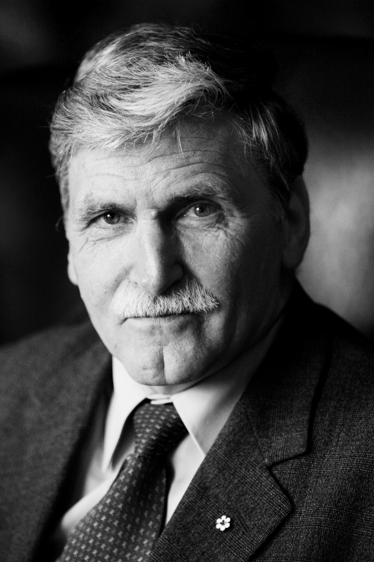 Black and white portrait of an older man with grey hair and mustache wearing a dark suit and tie.