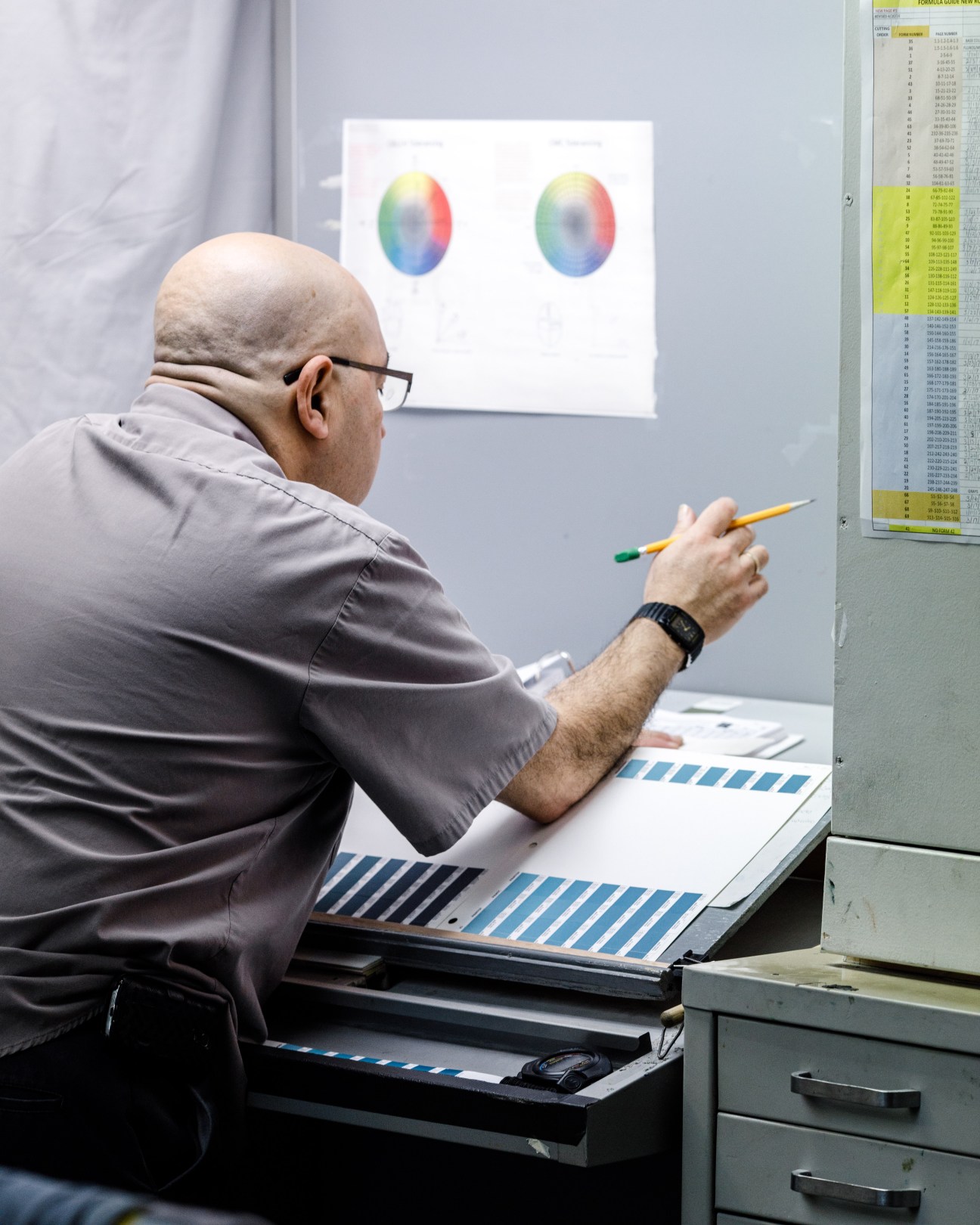 Man in gray shirt examining color swatches on a desk while viewing color spectrum display on wall