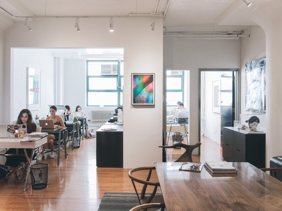 Interior of an open-plan office space with staff working at desks, framed artwork on walls, and modern furniture.