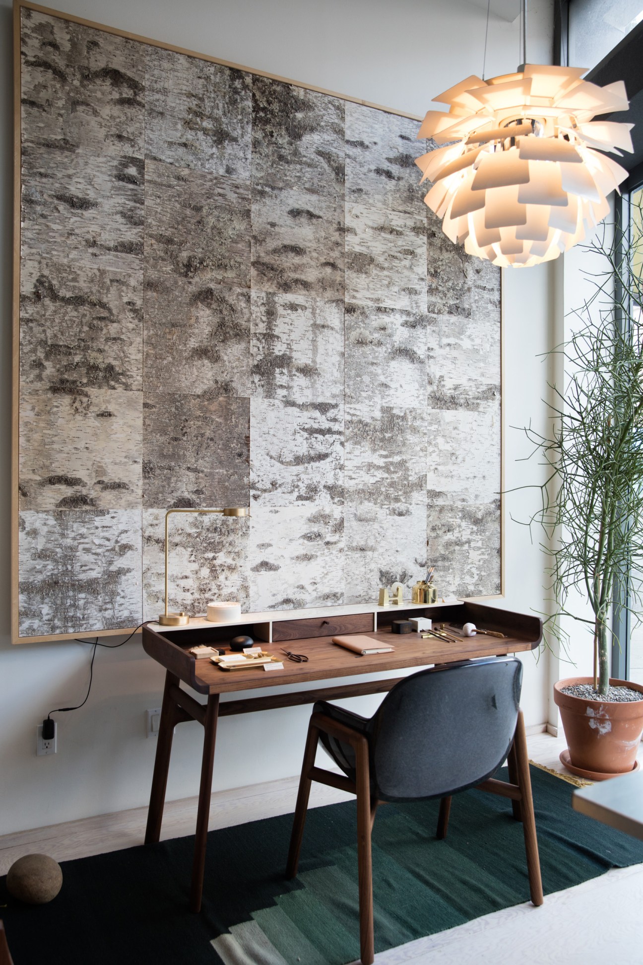 Modern wooden desk with chair, white pendant light, and large textured wall art in minimalist interior