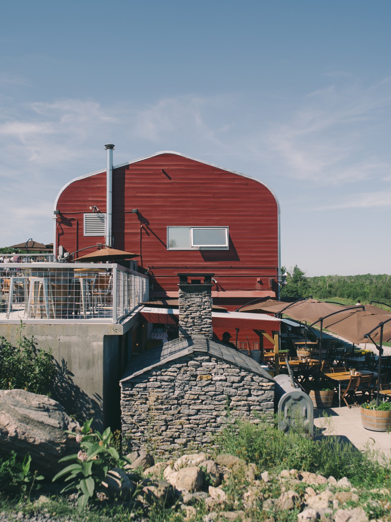 Red barn winery building with stone foundation and outdoor patio area at Norman Hardie vineyard