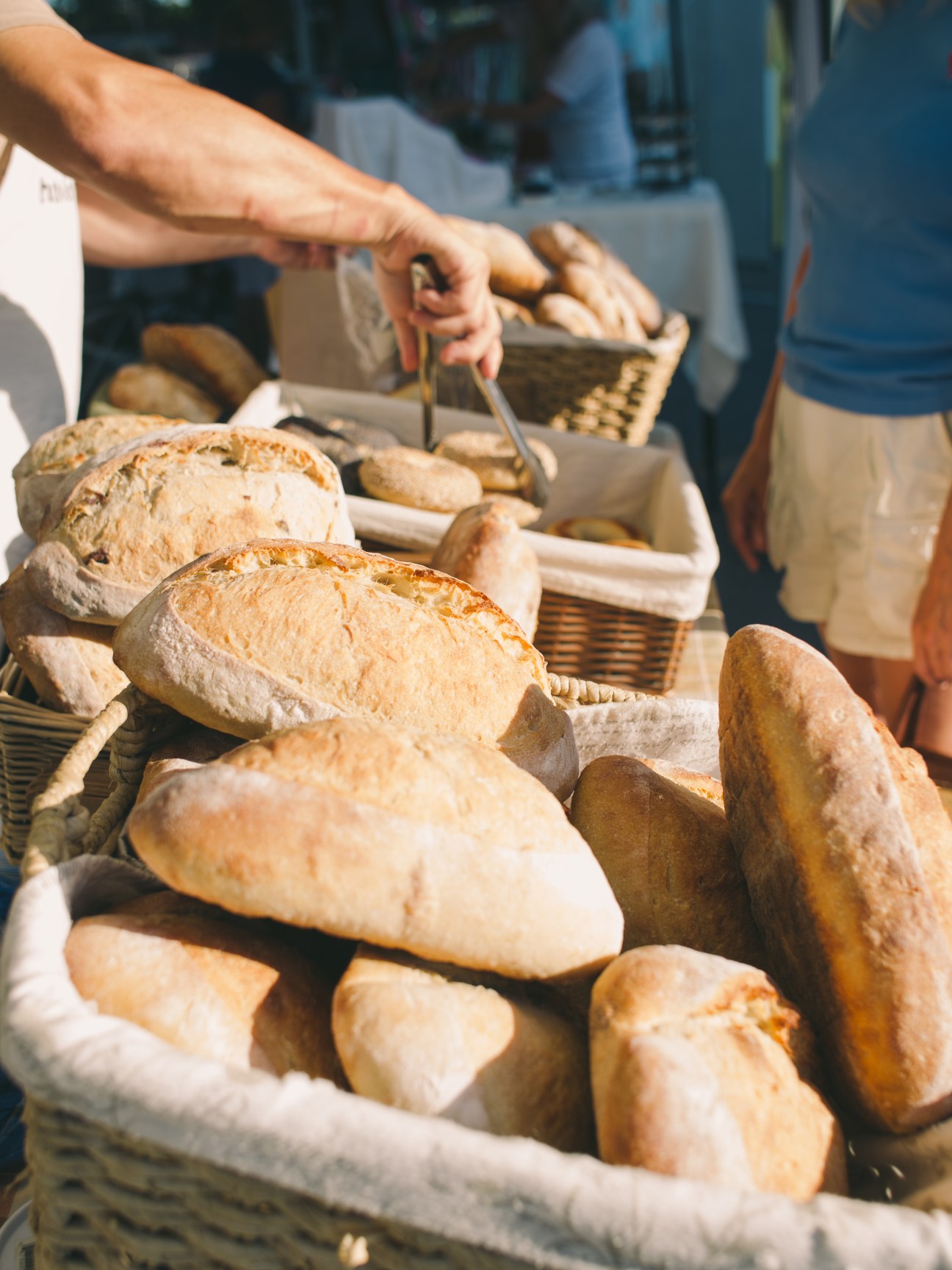 Hands selecting bread from wicker baskets filled with artisanal loaves at Humble Bread farmers market stand