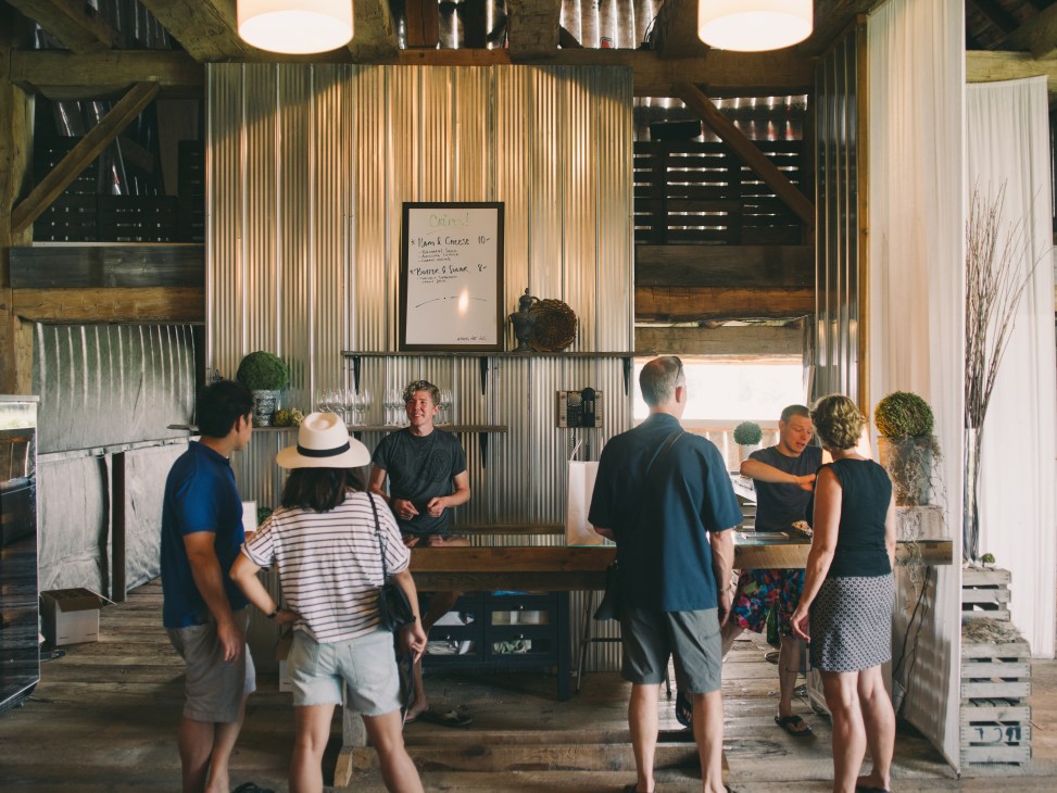 People gather around a rustic bar in The Old Third vineyard's corrugated metal and wood tasting room