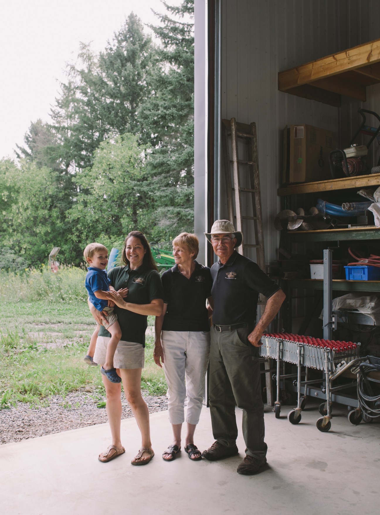 Four people standing together in a farm garage with shelving and equipment behind them