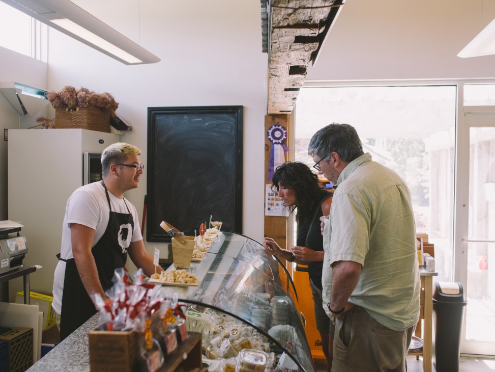 Three people taste cheese at a display counter in Fifth Town Artisan Cheese Co shop