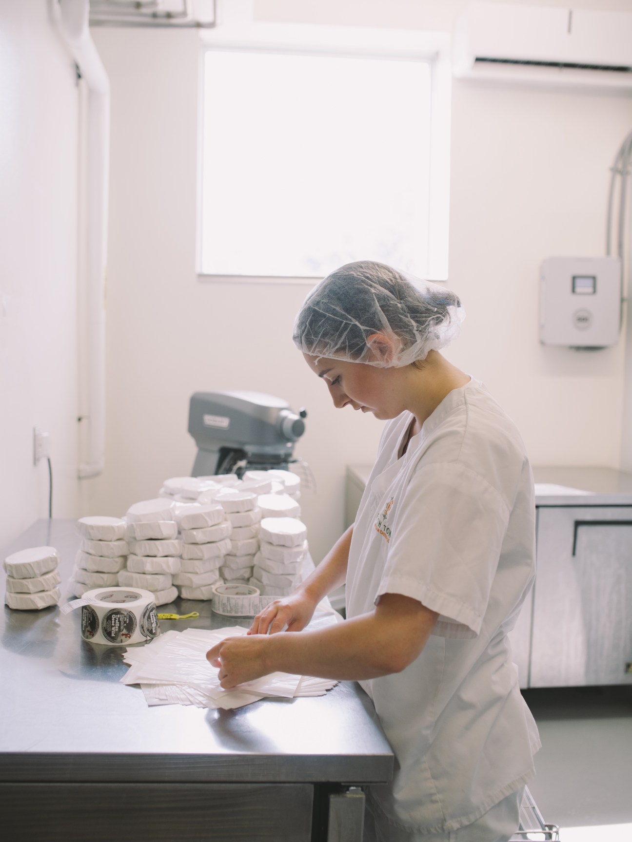 Worker in white uniform and hairnet packaging cheese rounds at Fifth Town Artisan Cheese Co