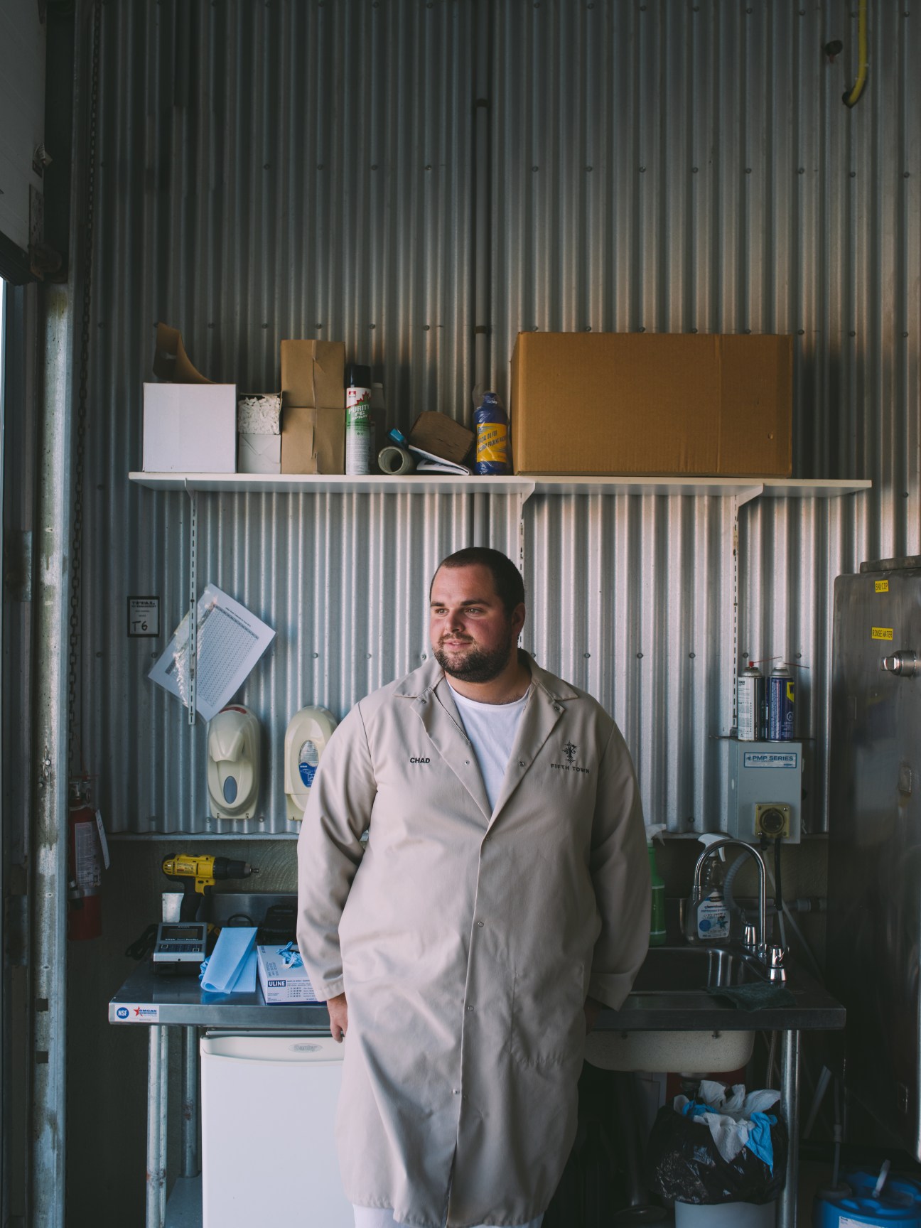 Chad Peterson in white lab coat standing in industrial kitchen workspace with metal shelving and equipment