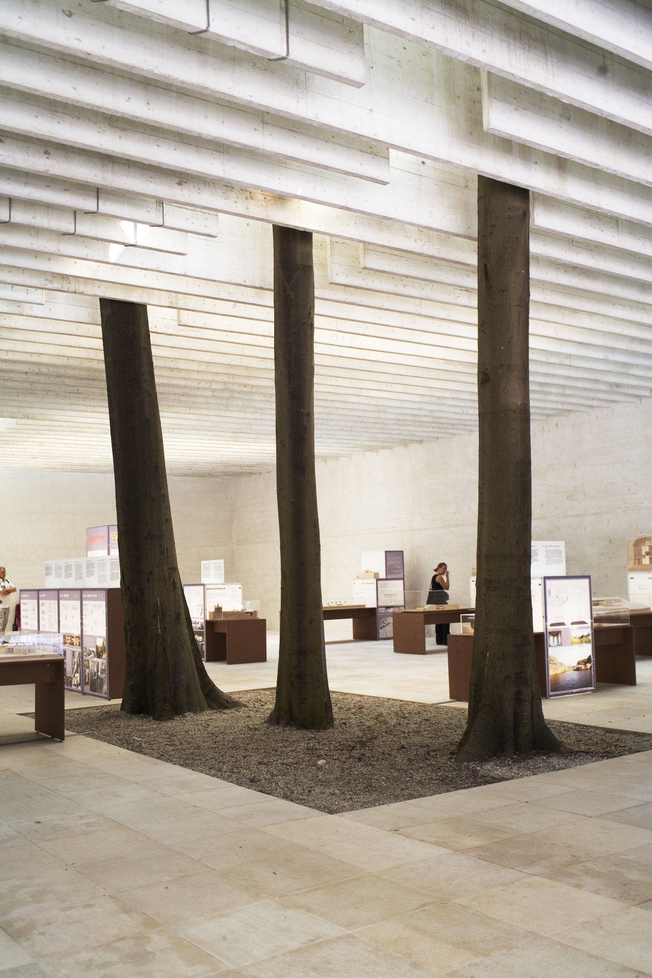 Interior of Nordic pavilion featuring three large wooden columns, exhibition displays, and minimalist architectural elements.
