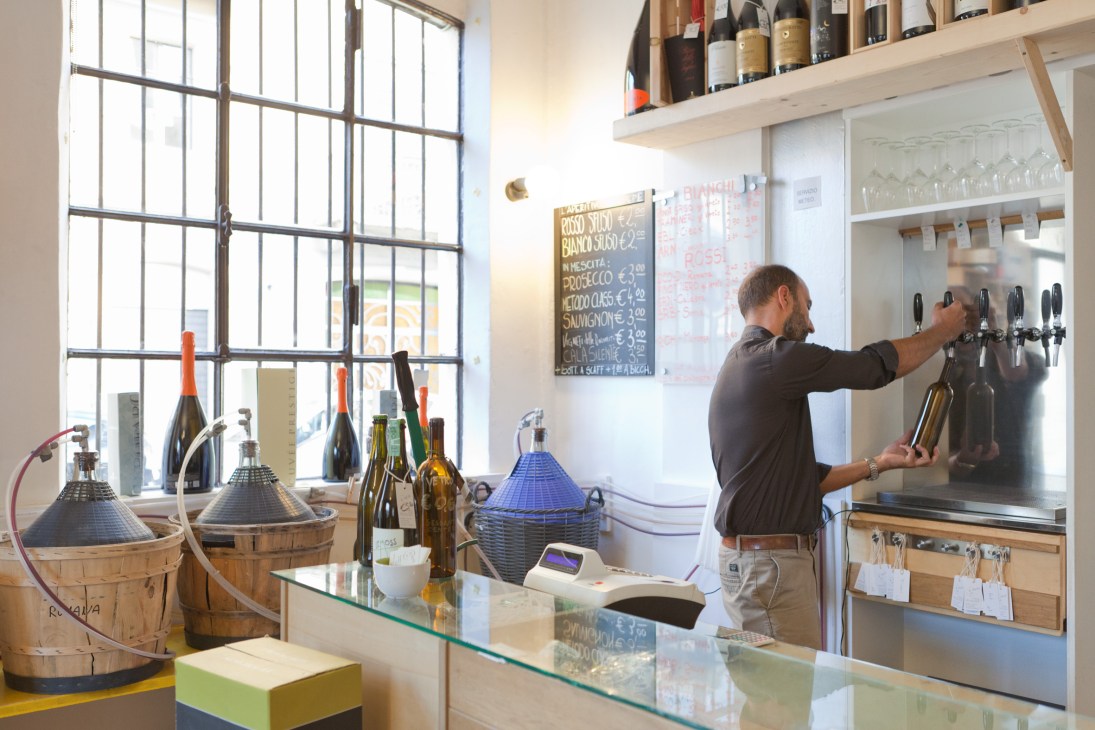 Man pouring wine at Depepe enoteca bar with shelves of bottles behind him.