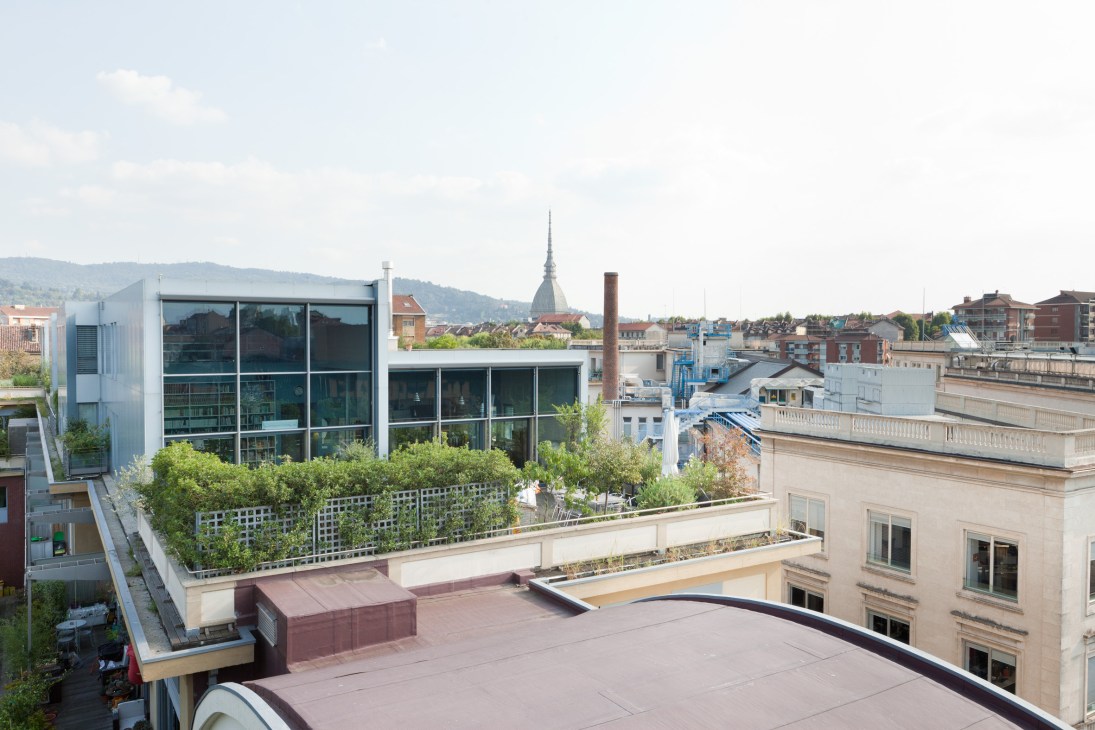 Rooftop terrace with planted boxes overlooking Turin's industrial skyline and Mole Antonelliana tower.