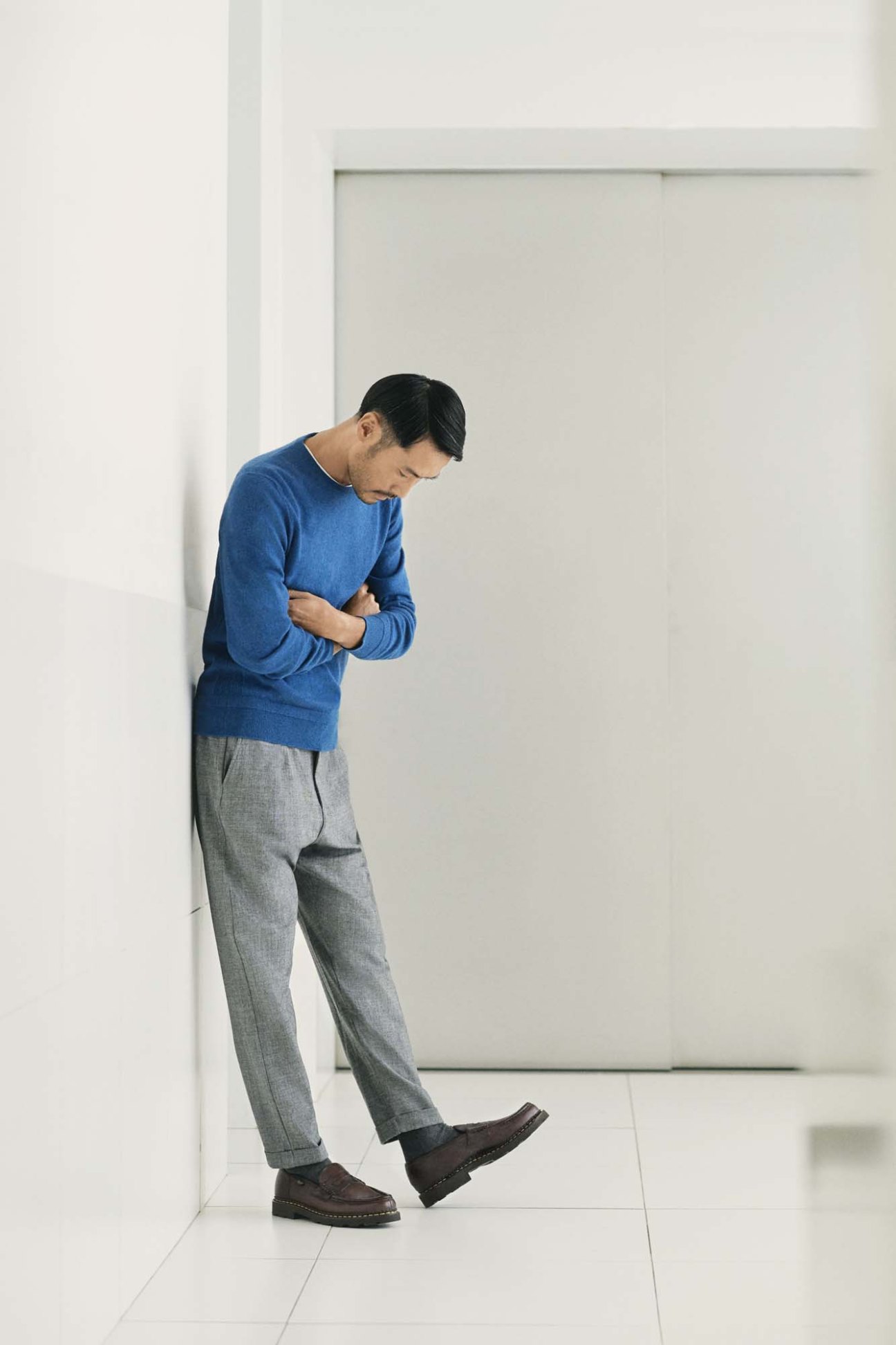 Man wearing blue Louis Vuitton jumper, gray Eleventy trousers, and Paraboot shoes against white wall.
