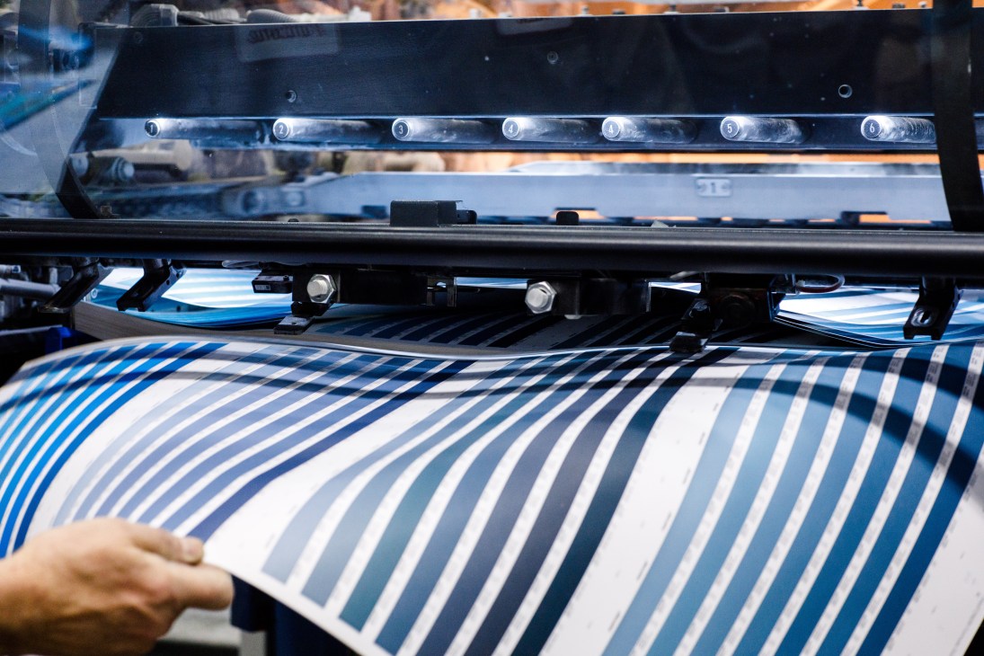 Industrial printing press with numbered color guides printing blue striped pattern on white material.