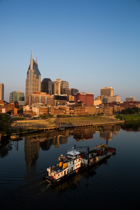 Barge on the Cumberland River with Nashville skyline and downtown buildings reflected in water.