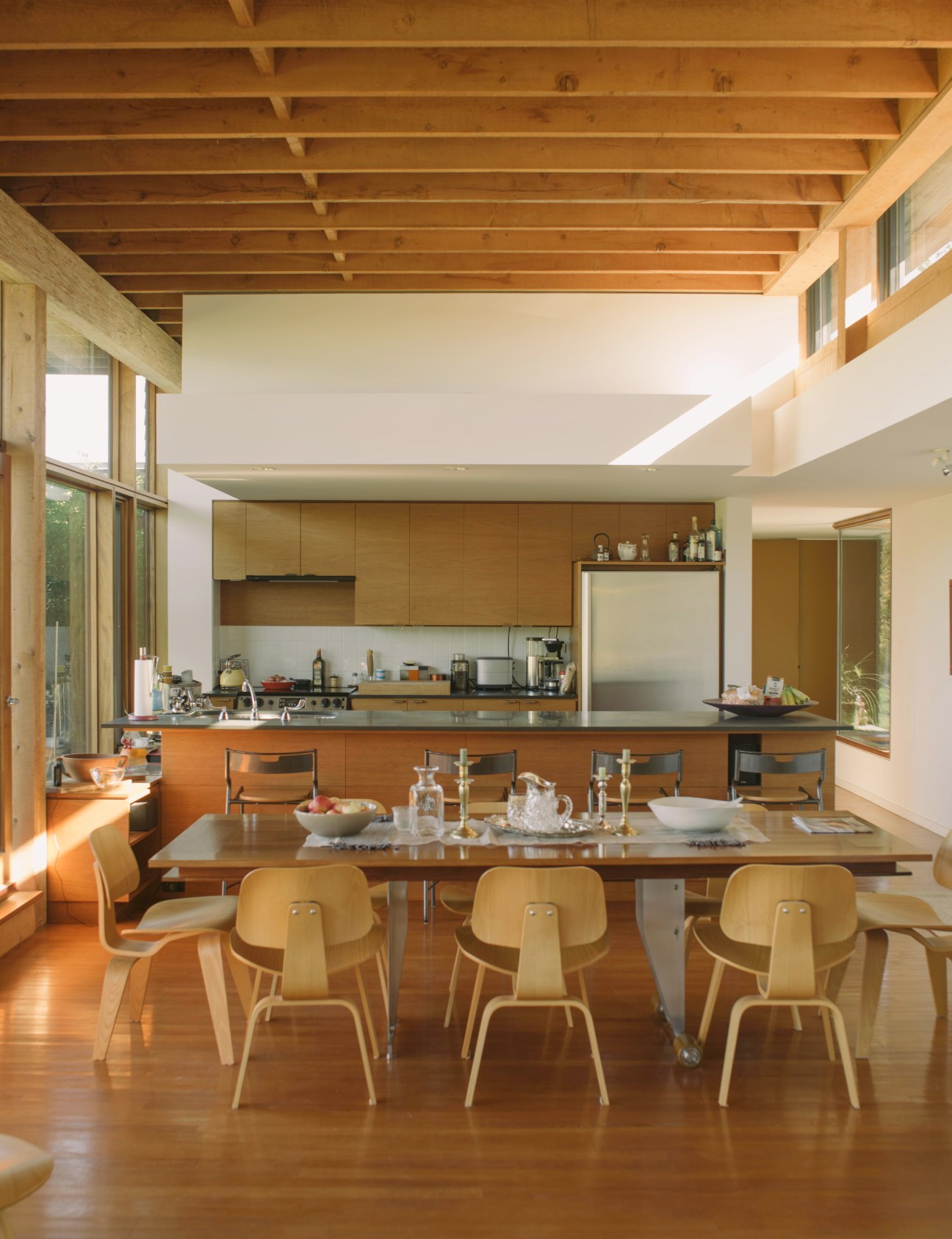 Modern kitchen with wood ceiling beams, stainless steel island, and blonde wood chairs around dining table