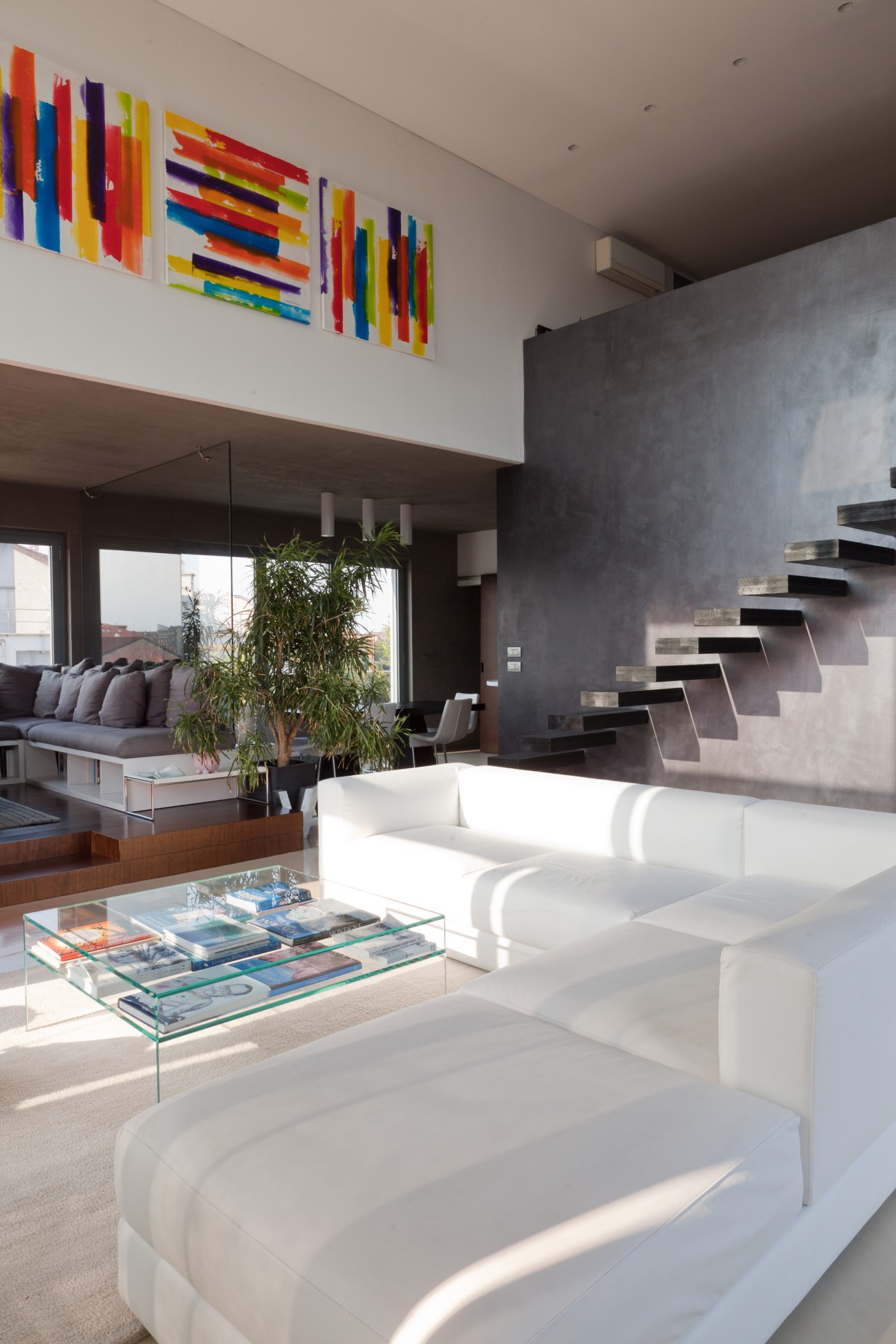 Modern loft interior with white curved sofa, floating stairs, and colorful abstract artwork on white walls.
