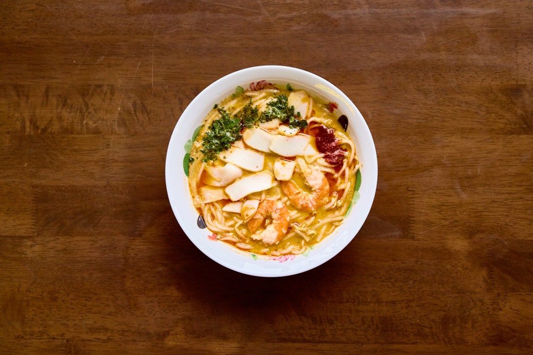 Bowl of laksa with noodles, broth, and toppings on wooden surface