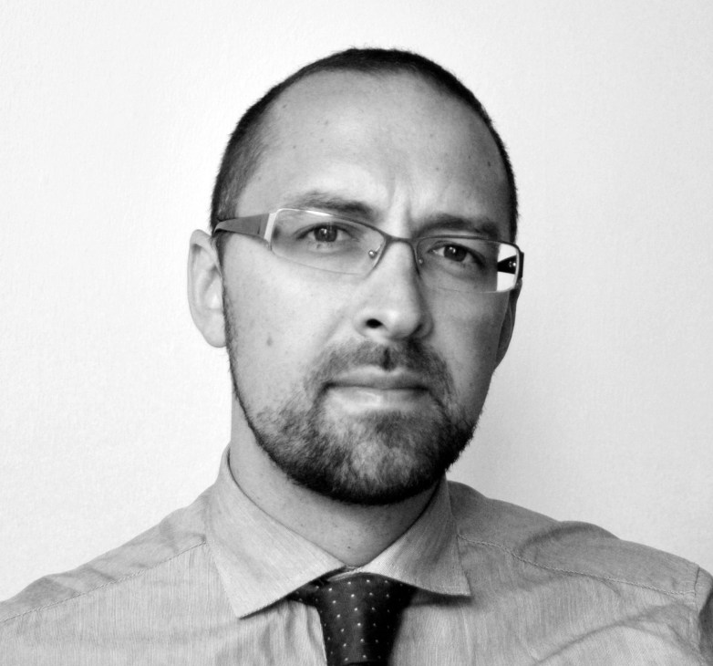 Black and white portrait photograph of a man wearing glasses, a light shirt and dark dotted tie.