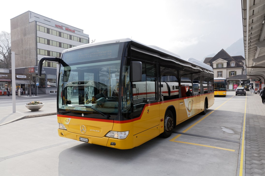 Yellow PostAuto bus with red stripe parked at a city bus station.